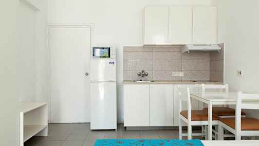 Et køkken med hvidt interiør, inklusive køleskab, mikrobølgeovn og spisebord med stole. (AI-genereret tekst)