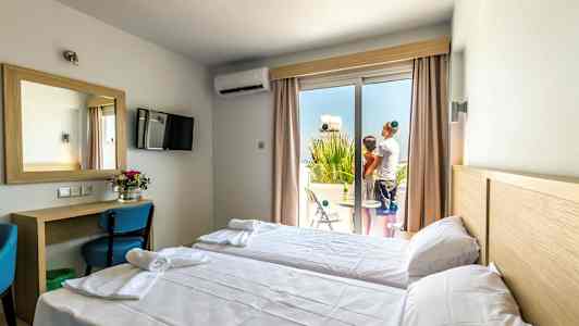 Hotelværelse med to enkeltsenge, skrivebord og spejl samt en altan med to personer. (AI-genereret tekst)