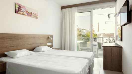 Dobbeltværelse med to enkeltsenge, en glasdør til altanen og et vægmonteret tv. (AI-genereret tekst)