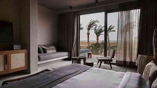 Et hotelværelse med en seng og udsigt over palmer uden for et glasvindue. (AI-genereret tekst)