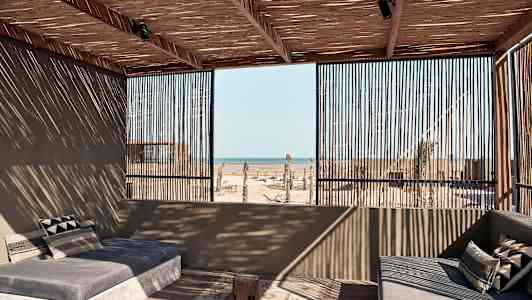 En åben terrasse med sofaer, hvor tag og vægge er lavet af træ, med udsigt til havet. (AI-genereret tekst)