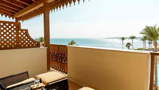 Altan med kurvemøbler og udsigt over havet og palmer. (AI-genereret tekst)