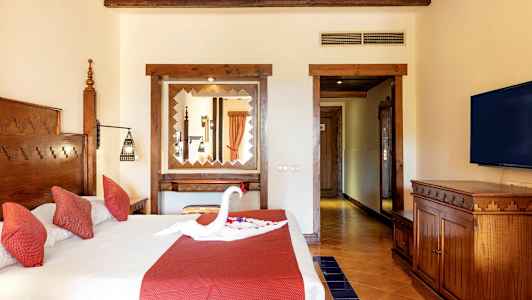 Et hotelværelse med en dobbeltseng med røde puder og en dekoration formet som en svane på sengen. (AI-genereret tekst)