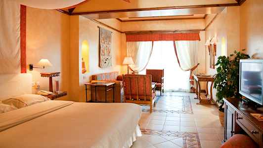 Et hotelværelse i varm indretningsstil med en stor seng, siddeområde, et tv og lysindfald fra vinduet. (AI-genereret tekst)