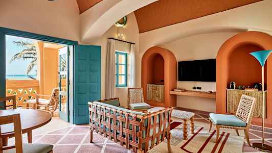 En indbydende stueindretning med farverige møbler, arkitektoniske buer og udsigt over havet gennem en åben dør. (AI-genereret tekst)