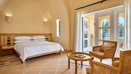 Et værelse med en seng, to stole og et bord samt en glasdør, der fører ud til en altan. (AI-genereret tekst)