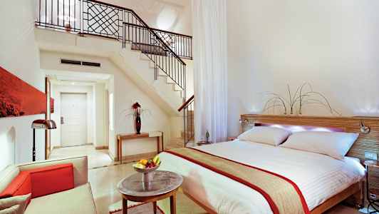 Moderne indrettet hotelsuite med dobbeltseng, siddeområde og trappe til hems. (AI-genereret tekst)