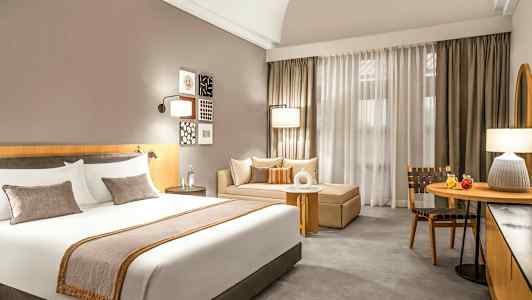 Billede af et hotelværelse med en stor seng, en sofa og et bord foran gardiner. (AI-genereret tekst)