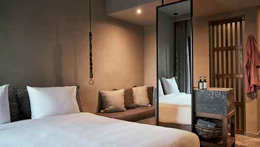 Et soveværelse med en stor seng, puder, en sofa og et højt spejl. (AI-genereret tekst)