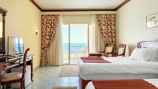 Hotelværelse med hvide vægge, to enkeltsenge og en balkon med udsigt til havet. (AI-genereret tekst)