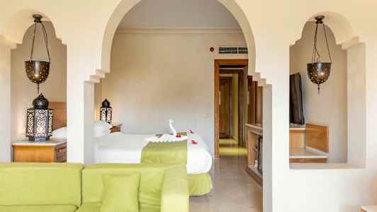 Stue med grøn sofa, soveværelse med to enkeltsenge, orientalske lamper og belyste detaljer. (AI-genereret tekst)