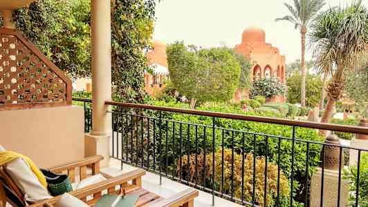 En terrasse med træstole og udsigt over en frodig have og en bygning med kuppel. (AI-genereret tekst)