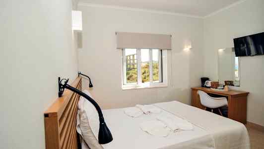 Et hotelværelse med en seng, vindue, skrivebord, stol og TV. (AI-genereret tekst)