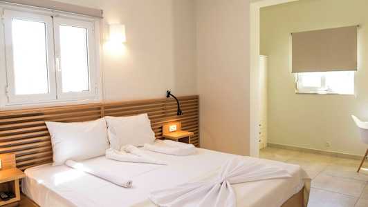 Et hotelværelse med en dobbeltseng, træpaneler som sengegavl, og en vindueslampe oven over. Et lille bord med en læselampe og en åbning til en anden del af rummet. (AI-genereret tekst)