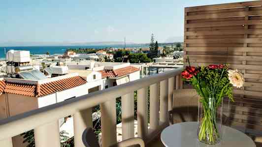 Udsigt fra altan med møbler, blomster på bordet og havet i baggrunden. (AI-genereret tekst)