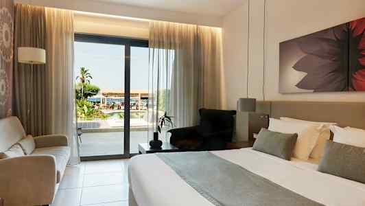 Hotelværelse med dobbeltseng og udsigt til udendørsområdet gennem en glasdør. (AI-genereret tekst)