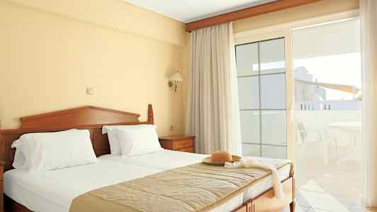 Et hotelværelse med en dobbeltseng, lyse gardiner og en altan med havemøbler. (AI-genereret tekst)