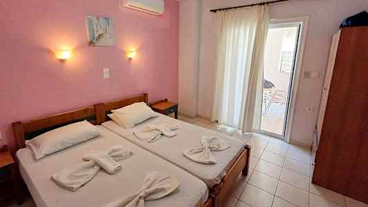 To enkeltsenge med hvidt sengetøj i et rum med rosa vægge og en glasdør, der fører ud til en altan. (AI-genereret tekst)