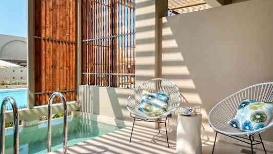 To stole med puder står ved et lille poolområde tæt på træpaneler. (AI-genereret tekst)