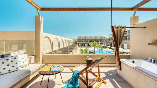 Terrasse med siddepladser, et badekar og udsigt over en pool og bygninger. (AI-genereret tekst)