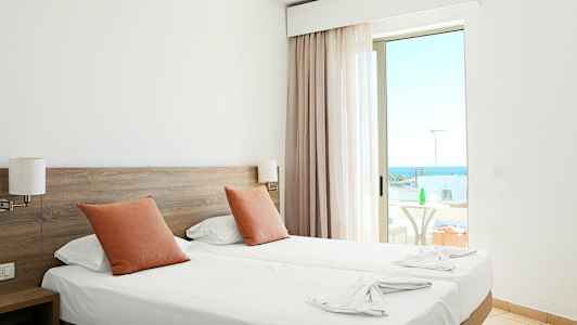 Hotelværelse med to enkeltsenge, orange puder og en altan med havudsigt. (AI-genereret tekst)