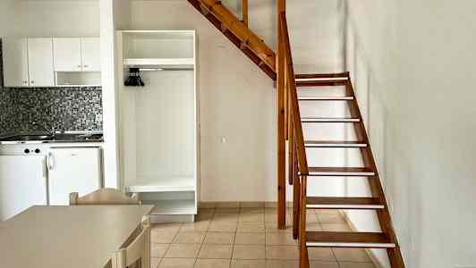 Indendørs billede med et lille køkken, et skab og en trætrappe til en hems. (AI-genereret tekst)