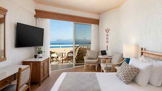 Et hotelværelse med en seng, siddeområde og en balkon med udsigt over havet. (AI-genereret tekst)