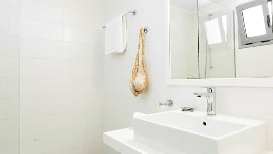 Et lyst badeværelse med hvide fliser på væggen, håndvask, håndklædeholder og spejl. (AI-genereret tekst)