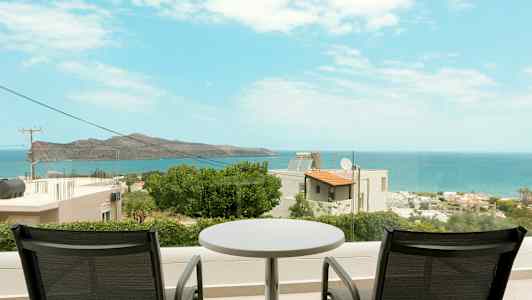 To stole og et bord på en altan med udsigt over havet og kystlandskabet. (AI-genereret tekst)