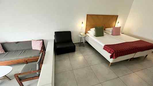 Et hotelværelse med seng, lænestol og sidemøbel. (AI-genereret tekst)