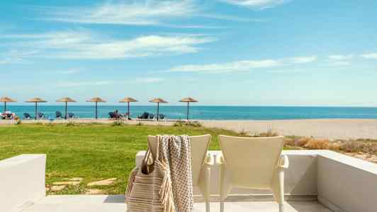 En strand med liggestole og parasoller med havet i baggrunden, en terrasse med stole i forgrunden. (AI-genereret tekst)
