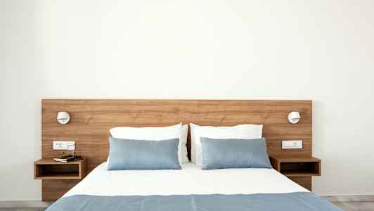 Seng med blåt sengetæppe og puder, træborde ved hver side. (AI-genereret tekst)