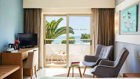 Hotelværelse med siddeområde og udsigt til altan med bord og stole samt havudsigt. (AI-genereret tekst)