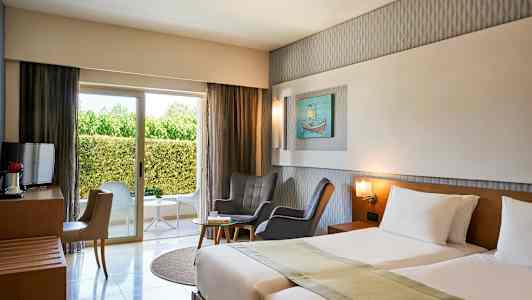 Hotelværelse med to senge, siddegruppe, vindue mod grønne omgivelser. (AI-genereret tekst)