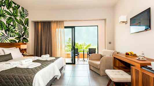 Et hotelværelse med dobbeltseng, siddegruppe, altan og vægdesign med bladmotiv. (AI-genereret tekst)