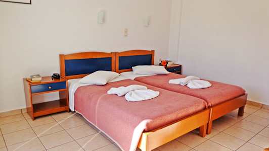 To enkeltsenge med foldede håndklæder og rosa sengetæppe, to natborde og flisegulv i et hotelværelse. (AI-genereret tekst)