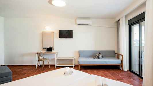 Et hotelværelse med en seng, sofa, skrivebord og en altan med glasdøre. (AI-genereret tekst)