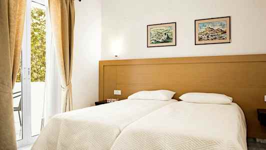 Et soveværelse med to enkeltsenge, en trækarm, lyse lagner og to malerier over sengene. (AI-genereret tekst)