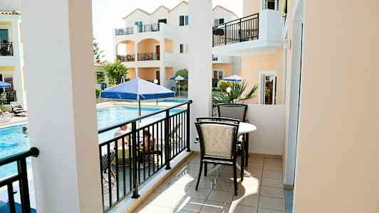 En balkon med møbler, udsigt over en pool og orange bygninger. (AI-genereret tekst)