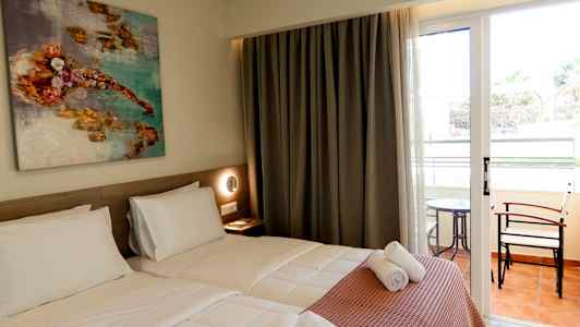 Et hotelværelse med to enkeltsenge, et kunstmaleri på væggen og glasdøre, der fører til en balkon med bord og stole. (AI-genereret tekst)