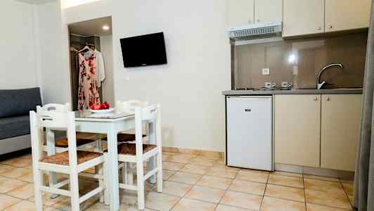 Et lille køkken med køkkenvask, køleskab og spisebord med fire stole samt en sofa og vægmonteret TV. (AI-genereret tekst)