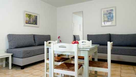 Et rum med to grå sofaer, et hvidt spisebord og fire stole. (AI-genereret tekst)