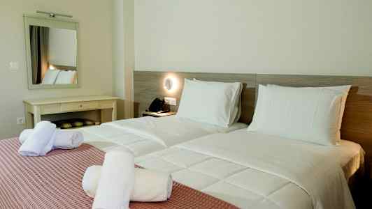 To enkeltsenge med hvidt sengetøj og rosa sengetæppe samt hvide rullede håndklæder ovenpå. (AI-genereret tekst)