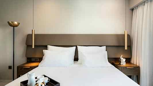 Et soveværelse med en dobbeltseng, hvide sengelinned og en bakke med teartikler på sengen. Lamper og natborde er på begge sider. (AI-genereret tekst)