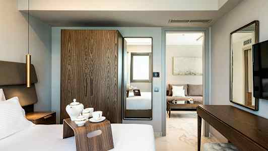 Et hotelværelse med seng, tebakke, garderobeskab og spejl. I baggrunden kan man se et opholdsområde med sofa. (AI-genereret tekst)