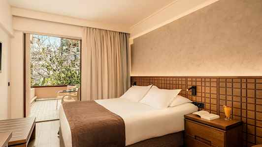 Hotelværelse med en dobbeltseng og en glasdør, der fører til en møbleret altan. (AI-genereret tekst)