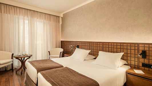 Et hotelværelse med to enkeltsenge, brun indretning og en lille siddegruppe. (AI-genereret tekst)