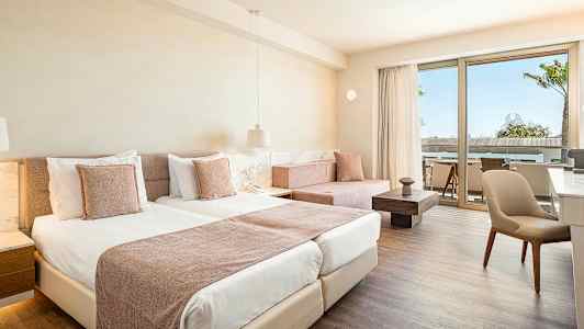 Værelse med lys indretning, to senge og en siddegruppe ved en terrasse. (AI-genereret tekst)