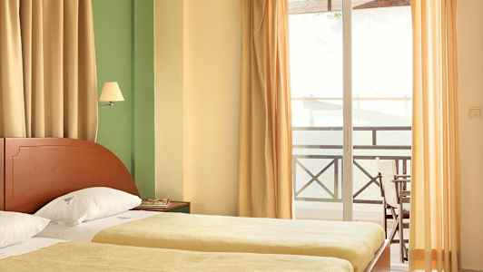 Et hotelværelse med to enkeltsenge, gardiner og en altan. (AI-genereret tekst)