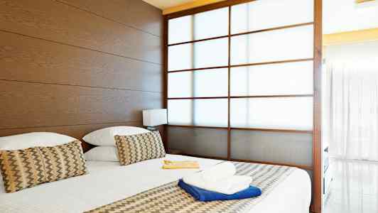 Et hotelværelse med en stor seng, træpaneler og en delvist gennemsigtig skydedør. (AI-genereret tekst)